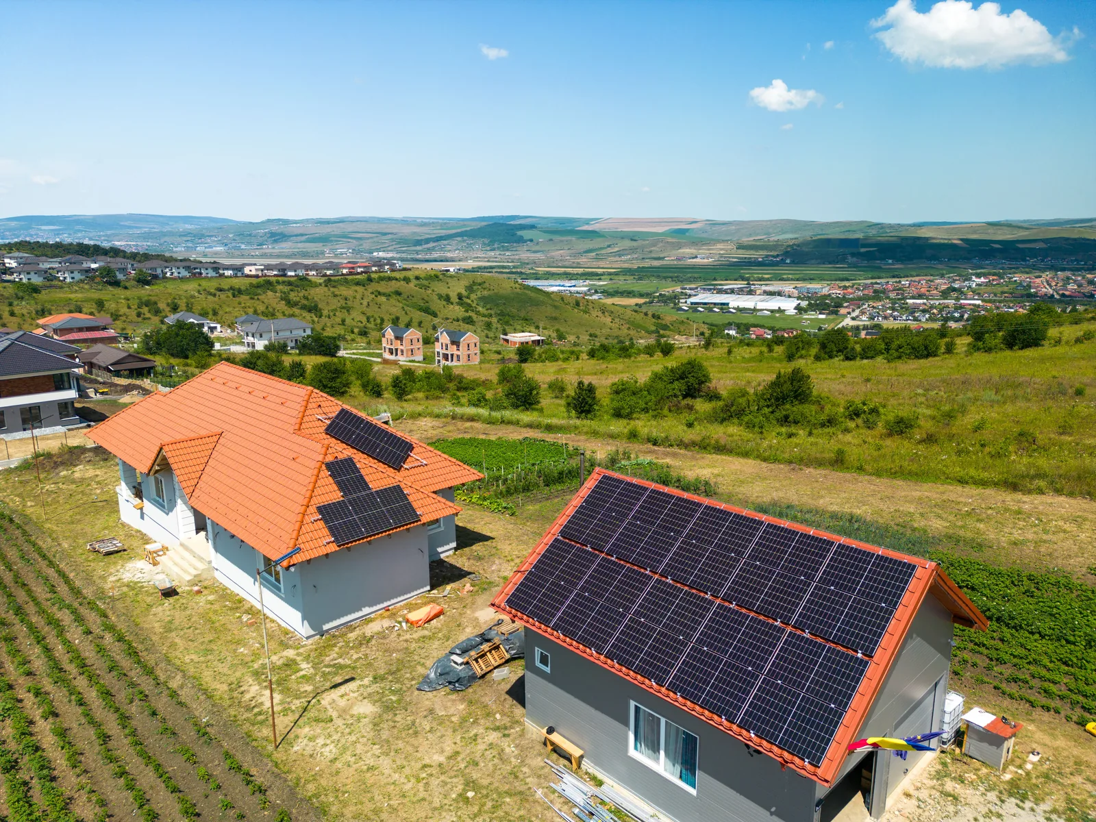 Două locuințe cu sisteme fotovoltaice montate pe acoperiș, cu valea și dealurile Clujului în fundal